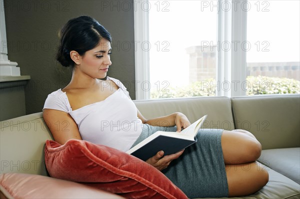 Mixed race woman reading book on sofa