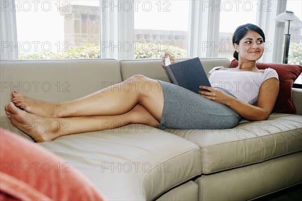 Mixed race woman reading book on sofa