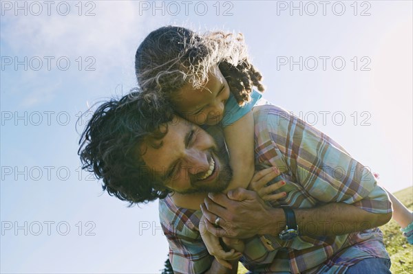 Low angle view of father carrying daughter piggyback outdoors