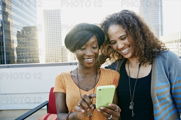 Women using cell phone together on urban rooftop