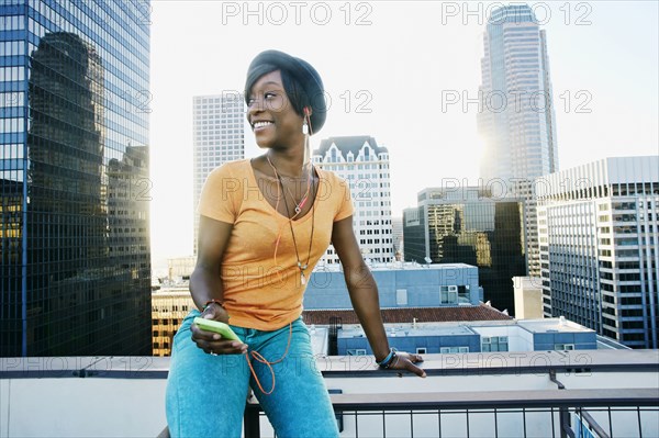 Black woman listening to earbuds on urban rooftop