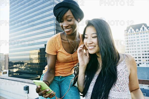 Women listening to earbuds on urban rooftop