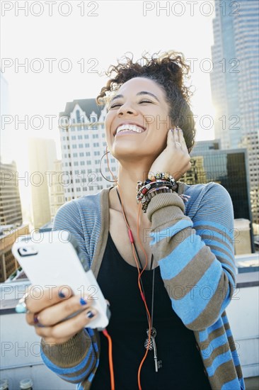 Mixed race woman listening to earbuds on urban rooftop