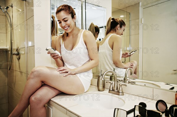 Caucasian woman using cell phone on bathroom counter