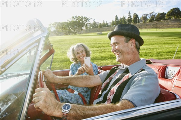 Couple taking cell phone photograph in classic convertible