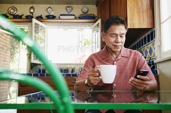 Filipino man using cell phone in kitchen