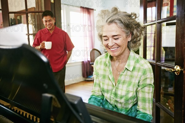 Man watching wife play piano in living room