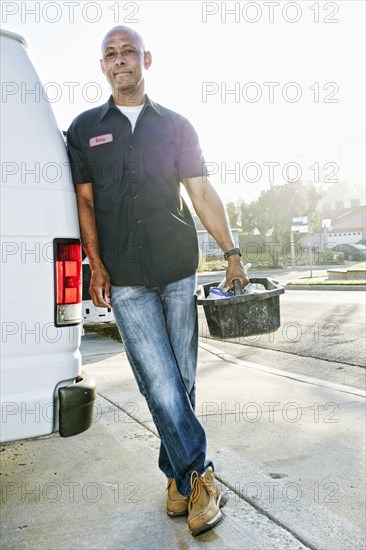 Mixed race plumber holding tools van