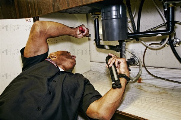 Mixed race plumber working under sink