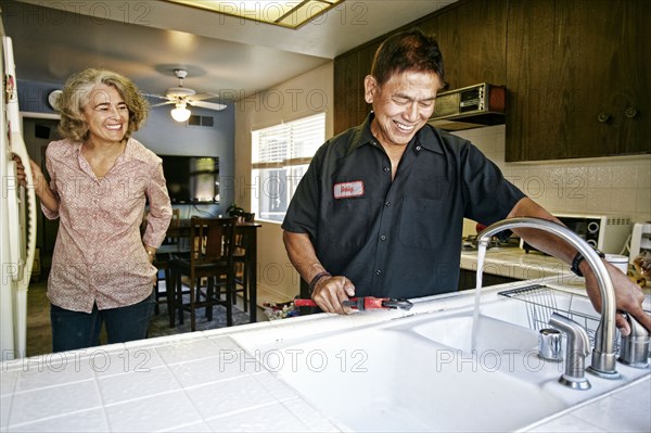 Plumber testing sink for woman in kitchen