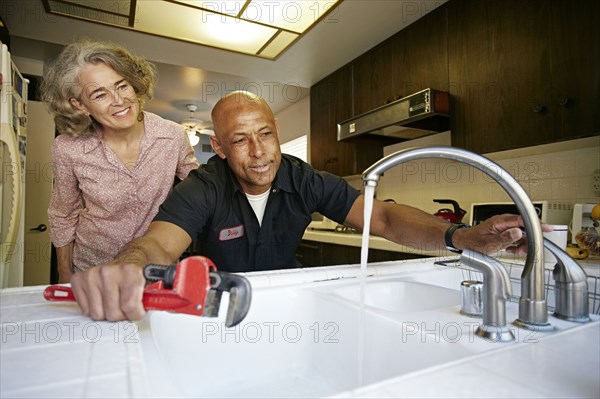 Plumber testing sink for woman in kitchen