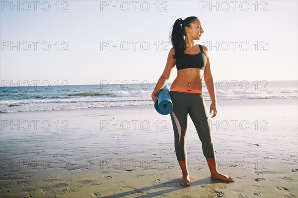 Mixed race woman holding yoga mat on beach