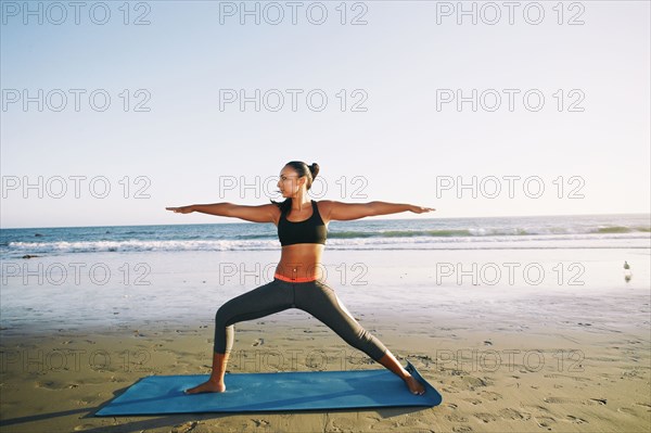 Mixed race woman practicing yoga on beach