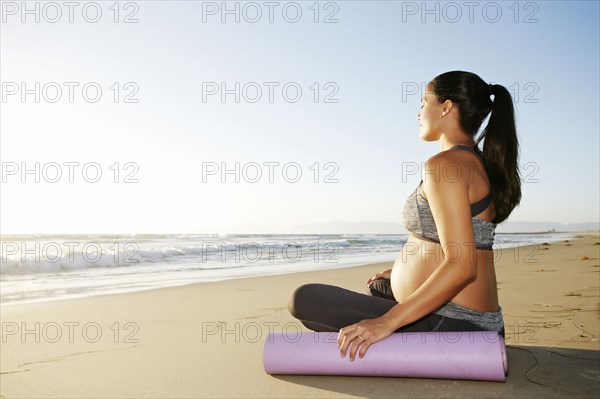 Pregnant Hispanic woman meditating on beach