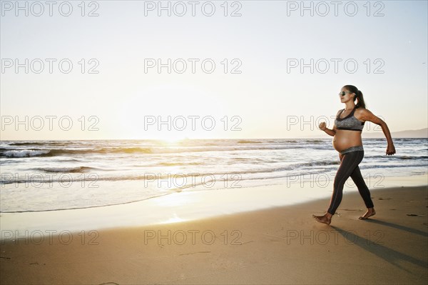 Pregnant Hispanic woman walking on beach