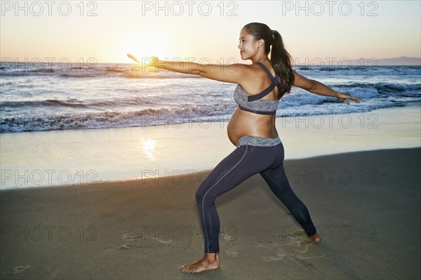 Pregnant Hispanic woman practicing yoga on beach