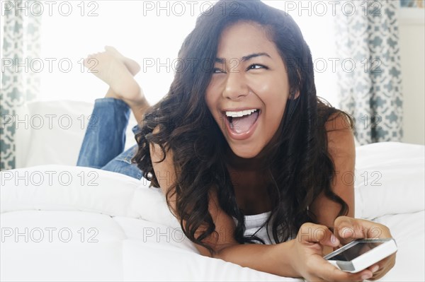 Hispanic woman using cell phone on bed