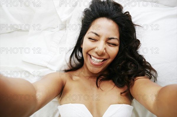 Hispanic woman taking selfie of herself on bed