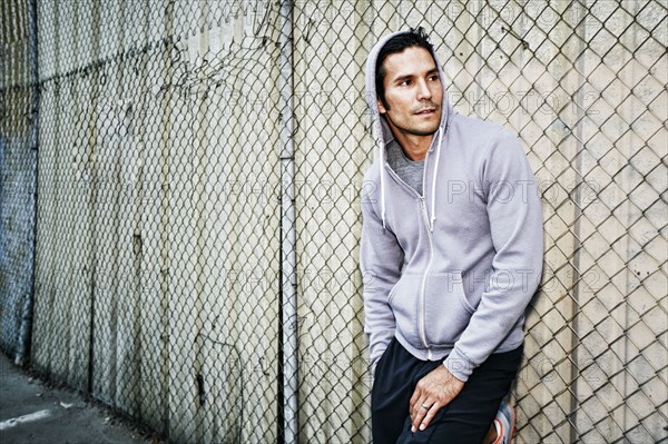 Mixed race man leaning on chain link fence