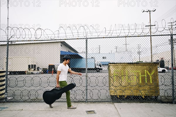 Mixed race musician carrying guitar case on sidewalk