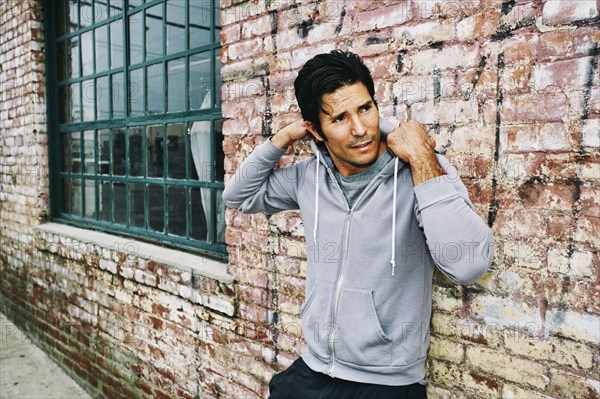 Mixed race man leaning on brick building