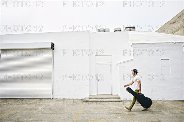 Mixed race musician carrying guitar case on sidewalk