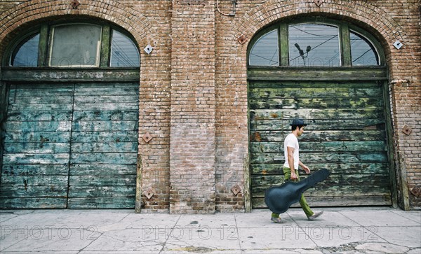 Mixed race musician carrying guitar case on sidewalk