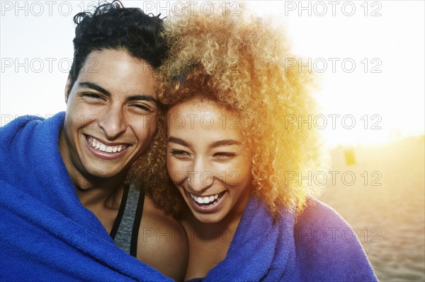 Hispanic couple wrapped in blanket on beach