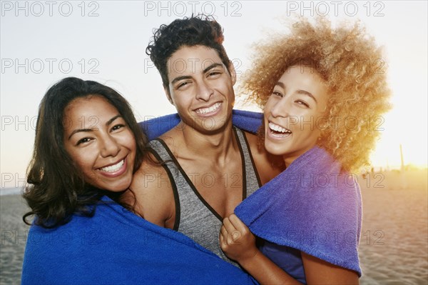 Hispanic friends wrapped in blanket on beach