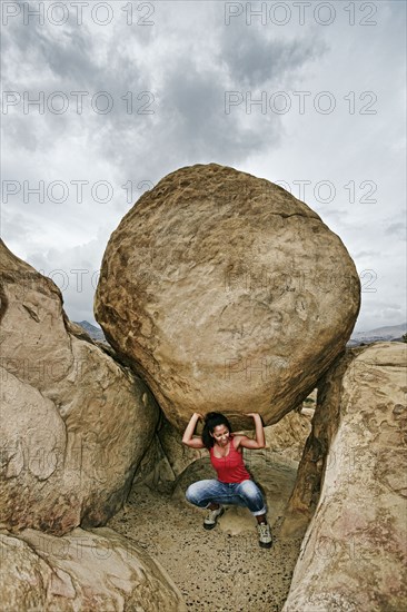 Hispanic woman lifting boulder on rocky hillside