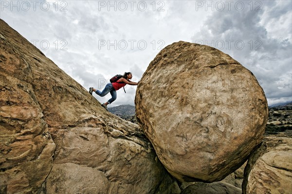 Hispanic woman pushing boulder on rocky hillside