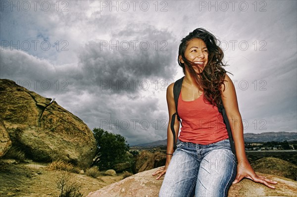Hispanic woman sitting on rocky hilltop