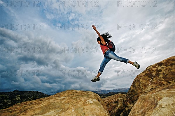 Hispanic woman jumping crevasse on rock formation