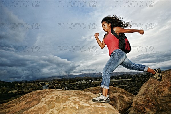 Hispanic woman jumping crevasse on rock formation
