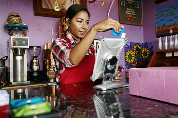 Hispanic barista using digital tablet register in coffee shop