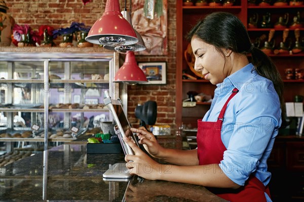 Hispanic cashier using digital tablet register in bakery
