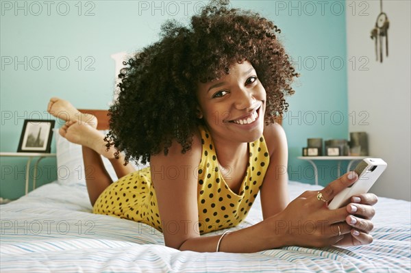 Smiling mixed race woman using cell phone on bed