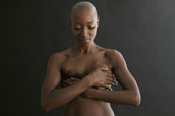 Nude African American cancer survivor covering her breasts