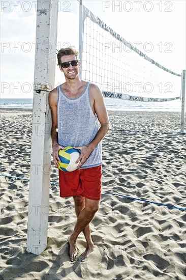 Caucasian man holding volleyball on beach