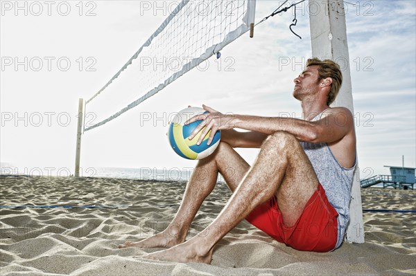 Caucasian man sitting near volleyball net on beach