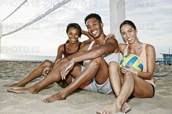 Friends sitting near volleyball net on beach