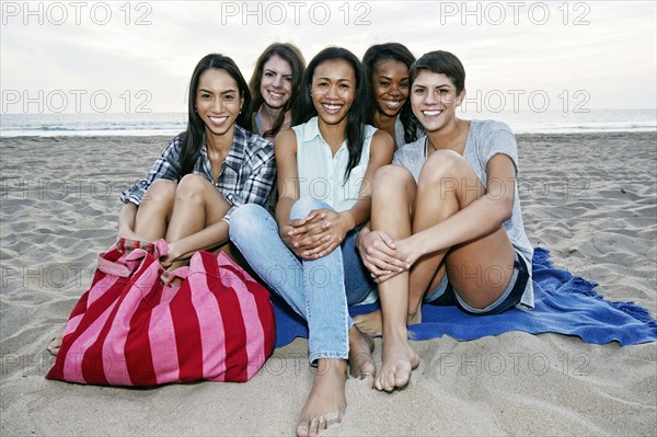 Smiling women sitting on blanket on beach