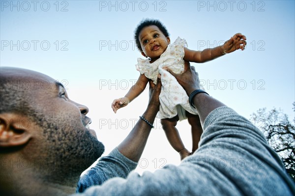 Black father holding baby daughter under blue sky