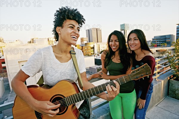 Woman playing guitar for friends on urban rooftop