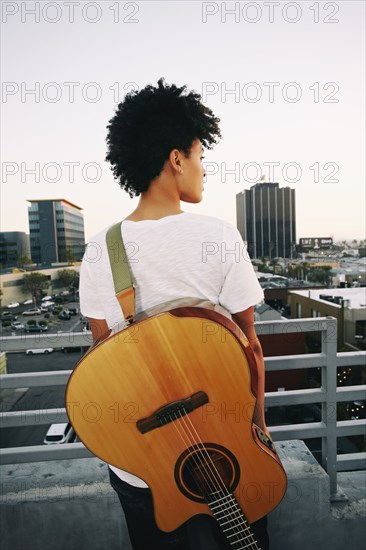 Woman wearing guitar on urban rooftop