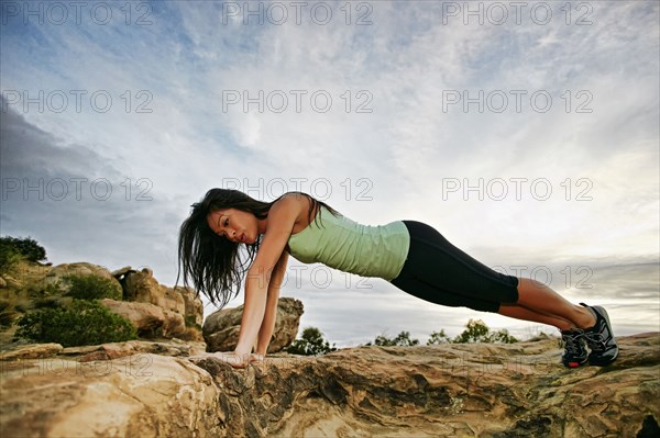 Vietnamese woman doing push-ups on rocky hilltop