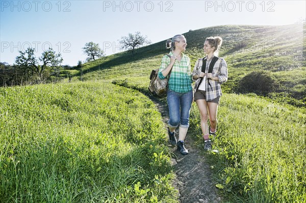 Caucasian mother and daughter walking on grassy hillside
