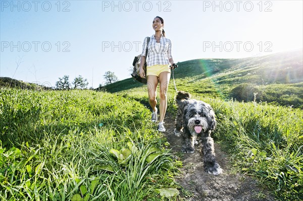 Mixed race woman walking dog on grassy hillside