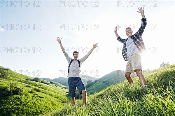 Caucasian father and son cheering on grassy hillside