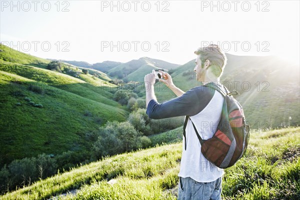 Caucasian man photographing scenic view from rural hilltop